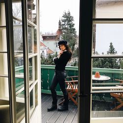 Full length portrait of young woman standing on balcony seen through doorway