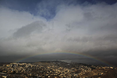 Rainbow over city against cloudy sky