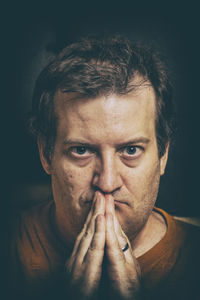 Close-up portrait of serious mature man with hands clasped against black background