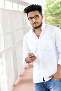 Portrait of man holding mobile phone while standing outdoors