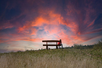 A person sits alone on a bench in nature, with a great sky