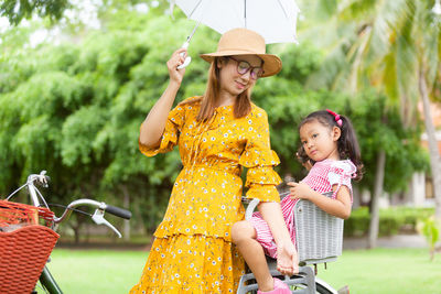 Woman with bicycle holding umbrella by daughter on land