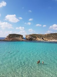 People swimming in blue-green sea against sky