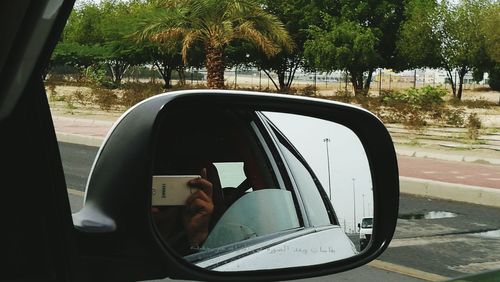 Reflection of man photographing on side-view mirror of car