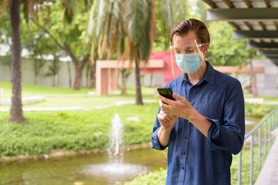 Man using mobile phone while standing by plants