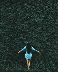 Rear view of carefree woman with arms outstretched standing against plants