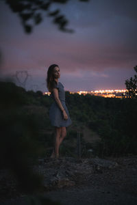 Side view of woman standing on field against sky at sunset