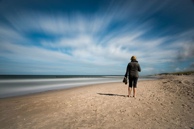 Rear view of woman walking on beach against sky