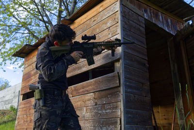 A young sniper aims at a house from the woods