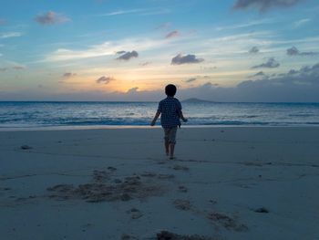 Rear view of man standing on beach against sky during sunset