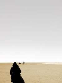 Rear view of silhouette people on beach against clear sky