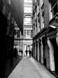 Rear view of people walking on footpath amidst buildings in city