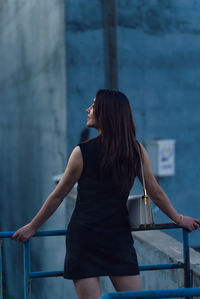 Young woman looking away while standing against wall