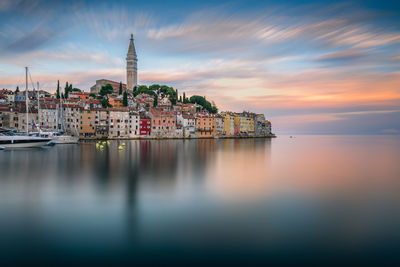 Buildings by sea against sky during sunset