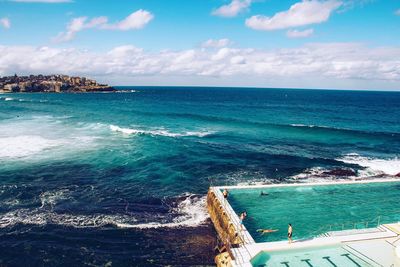 People swimming in infinity pool against seascape