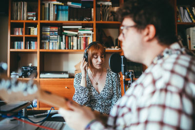 Blurred unrecognizable male guitarist playing guitar against female vocalist with professional microphone during rehearsal in house