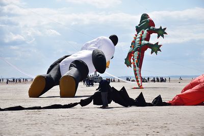 Man standing by inflatable kites at beach against sky