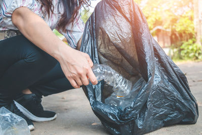 Low section of woman collecting garbage in plastic bag on road