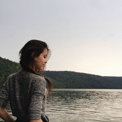Portrait of young woman by lake against sky