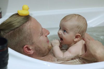 Father and daughter playing with rubber duck in bathtub