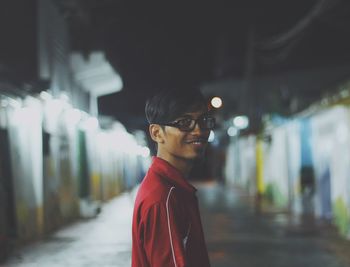 Side view of smiling young man standing on street at night