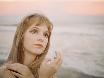 Thoughtful young woman looking away at beach during sunset