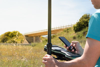 Land surveyor with a gps instrument, checking data with his smartphone