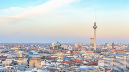 Fernsehturm amidst cityscape against sky during sunset