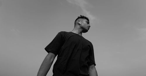 Low angle view of young man looking away against sky