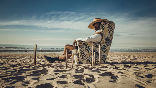 Man on chair at beach against sky