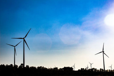 Low angle view of silhouette wind turbines on field against sky