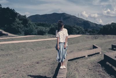 High angle view of woman standing on retaining wall at field against sky