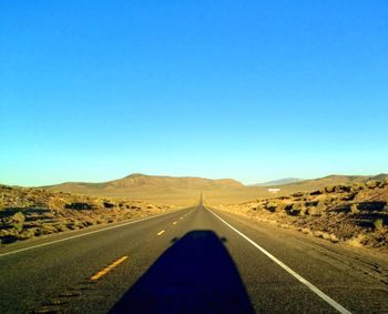 Empty road leading towards mountain against clear blue sky