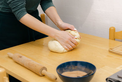 The hand of a caucasian young girl kneads dough on the table.