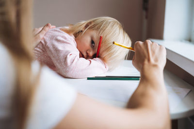 Little girl toddler with her mother drawing with colored pencils on table in children's room at home