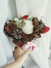 Cropped hand of woman holding bouquet against white curtain