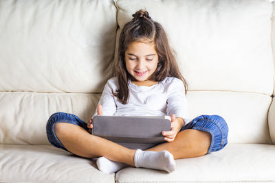 Smiling girl using digital tablet while sitting on sofa at home