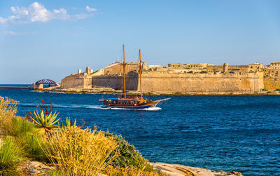 Sailboats moored on sea by buildings against sky