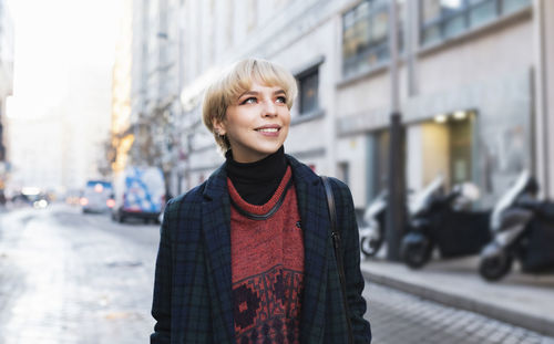 Portrait of smiling young woman standing on street in city