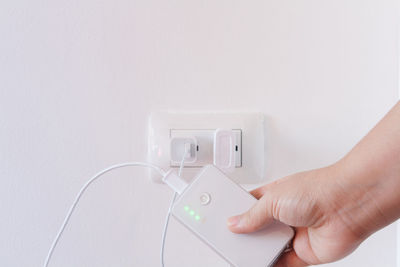 Cropped hand of man charging powerbank by white wall