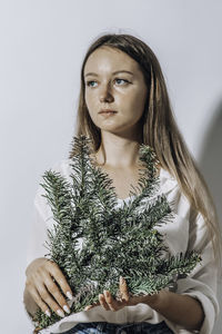 Young beautiful woman holding fir branches against white wall. minimalistic festive christmas new