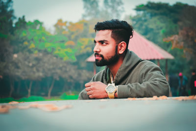 Young man looking away against trees