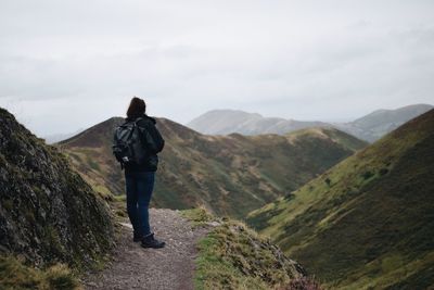 Rear view of hiker standing on trail against sky