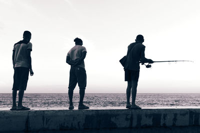 Silhouette men standing on beach against clear sky