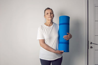 Woman aged athlete stands in a white room with a yoga mat