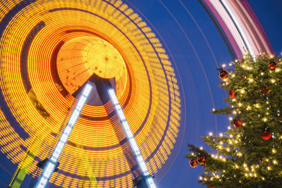 Low angle view of spinning ferris wheel by fernsehturm tower during christmas