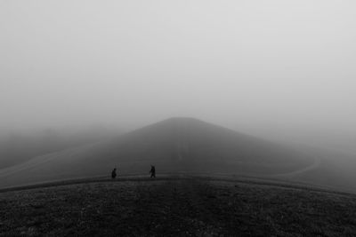 People on mountain against sky during foggy weather