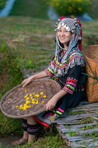 Woman holding hat while sitting by basket outdoors