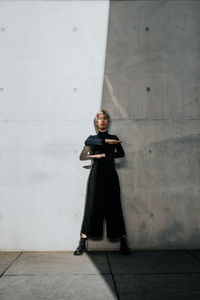 Portrait of young woman standing against wall