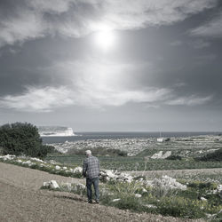 Rear view of man standing at beach against sky